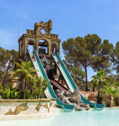 Wasserparadies mit zwei Rutschen und Palmen in der Umgebung.