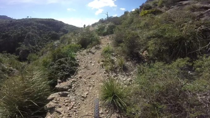 MTB Bike Station - Downhill Enduro - Santa Ponca Schmaler Wanderweg durch grüne Hügel mit ausgedehnten Landschaftsansichten.
