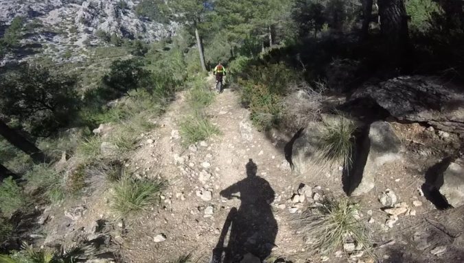 MTB Bike Station - Downhill Enduro - Santa Ponca Mountainbike-Strecke mit einem Fahrer auf schmalem Pfad zwischen Bäumen und Felsen.