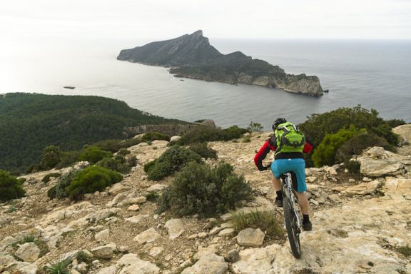 MTB Bike Station - Downhill Enduro - Santa Ponca Mountainbiker fährt auf einem schmalen Pfad mit Blick auf die Küste und das Meer.