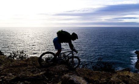 Radfahrer auf einem Felsen mit Blick auf das Meer bei Sonnenuntergang.