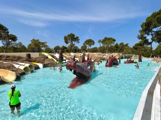 Personen spielen in einem Wasserpark mit Rutschen und einem blauen Pool.
