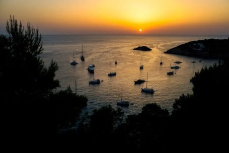 Sonnenuntergang über einer Bucht mit Segelbooten und ruhigem Wasser.