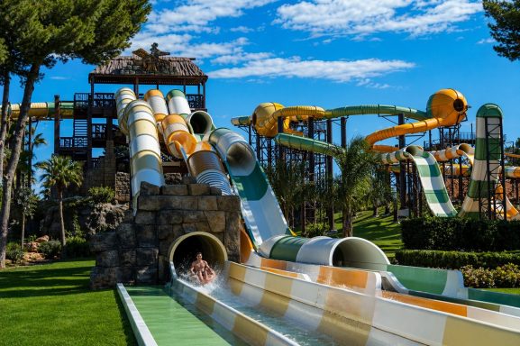 Wasserpark mit mehreren Rutschen und grüner Umgebung unter blauem Himmel.